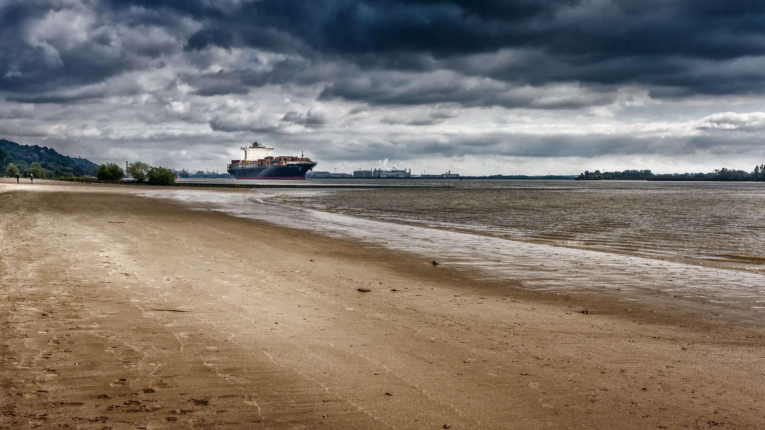 Strand in Hamburg mit Containerschiff im Hintergrund bei bewölktem Himmel